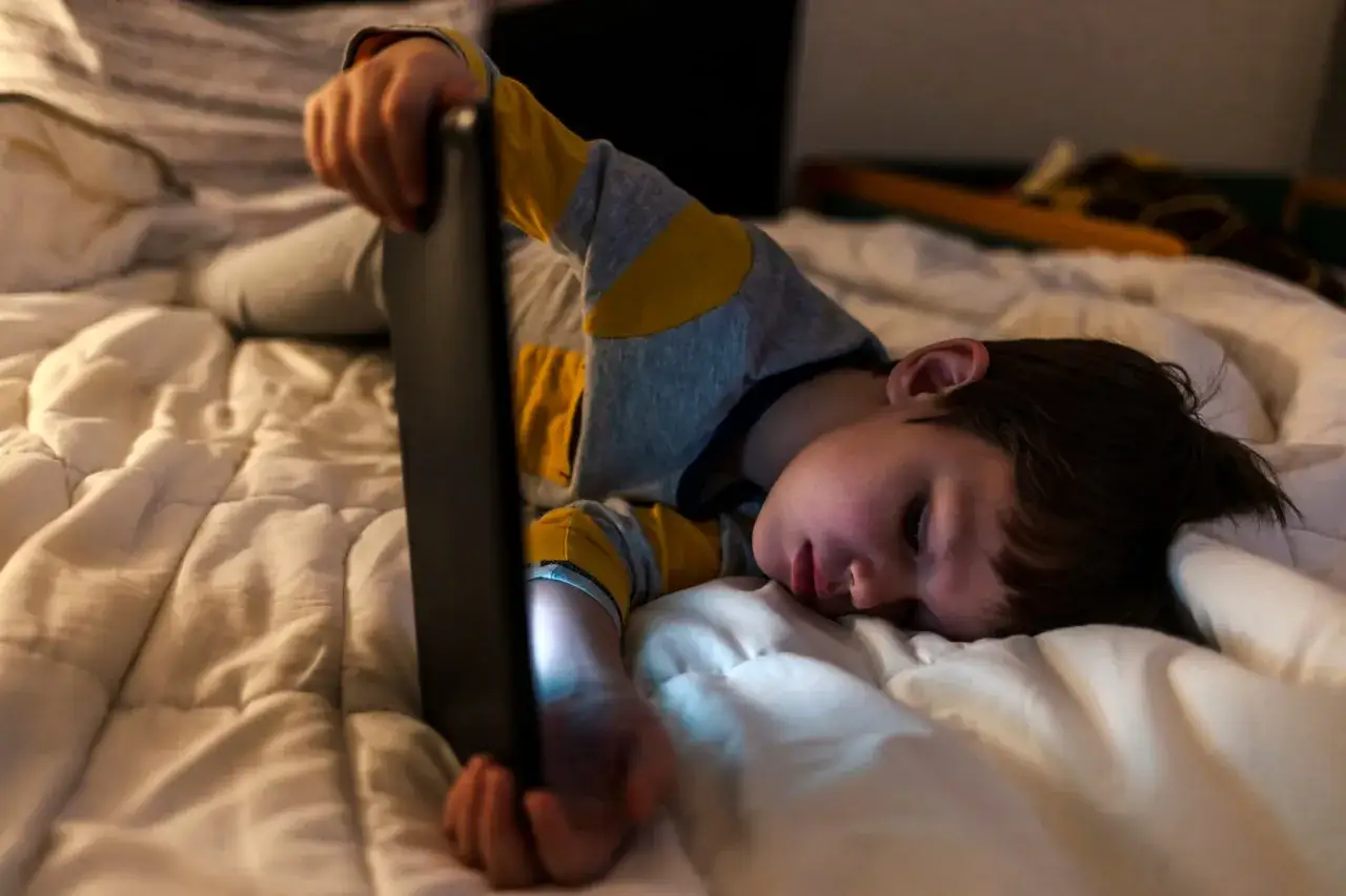 Niño de 2 años, con ojeras, mirando una tablet en la cama. Parece que mi hijo de 2 años se despierta mucho por la noche.