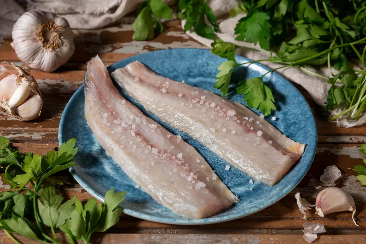 Filetti di merluzzo salati su piatto blu, con aglio e prezzemolo. Ideali per scoprire i merluzzo valori nutrizionali.