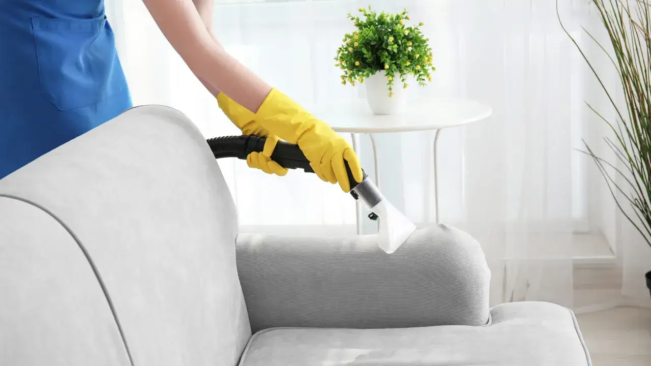 H&auml;nde in gelben Handschuhen reinigen mit einem Dampfreiniger die Polstergarnitur.