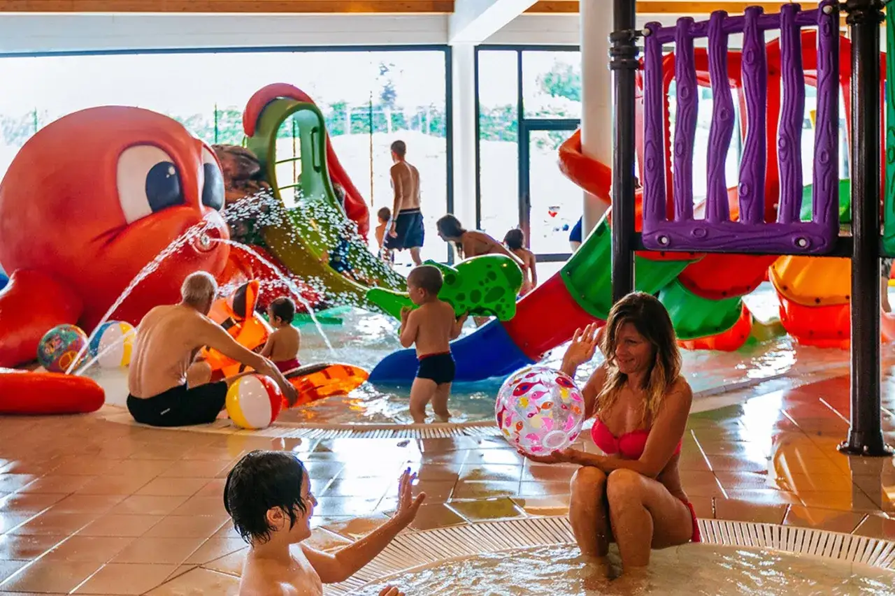 Bambini e adulti si divertono nelle **terme per bambini** con scivoli colorati e una grande attrazione a forma di polpo che spruzza acqua.