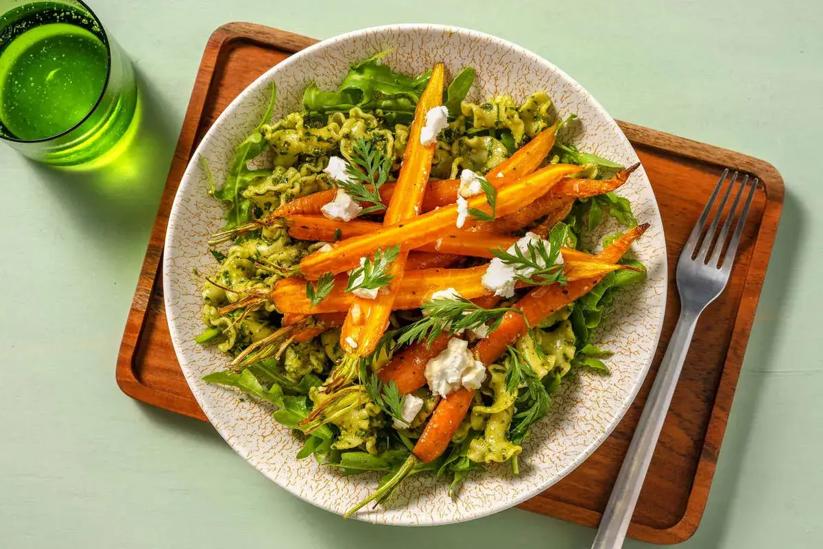 Un plat de p&acirc;tes aux fanes de carottes, fromage frais et herbes, servi avec un verre de boisson verte p&eacute;tillante.