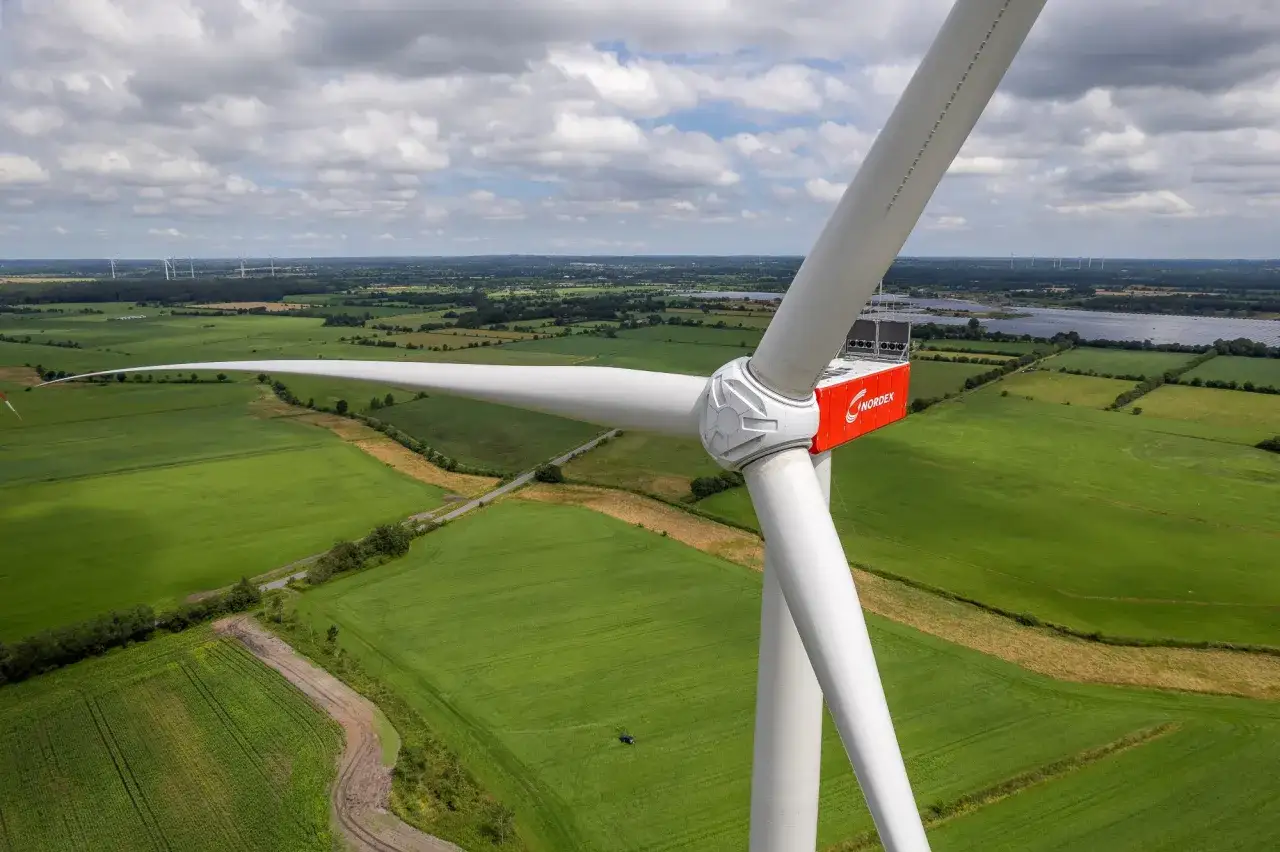 Nahaufnahme einer Windkraftanlage im **onshore windpark**. Grüne Felder und eine weite Landschaft erstrecken sich im Hintergrund.