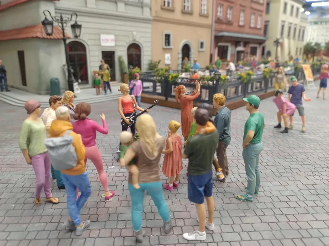 Miniaturowa scena z życia w **kolejkowo Warszawa**. Dziewczyna gra na gitarze, inni tańczą i bawią się na ulicy.