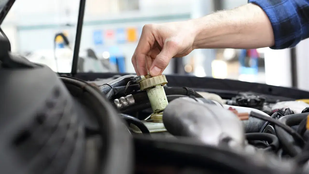 Ręka mechanika odkręca zakrętkę zbiorniczka płynu hamulcowego. Zaniedbanie wymiany płynu hamulcowego powyżej 2 lat może prowadzić do poważnych awarii.