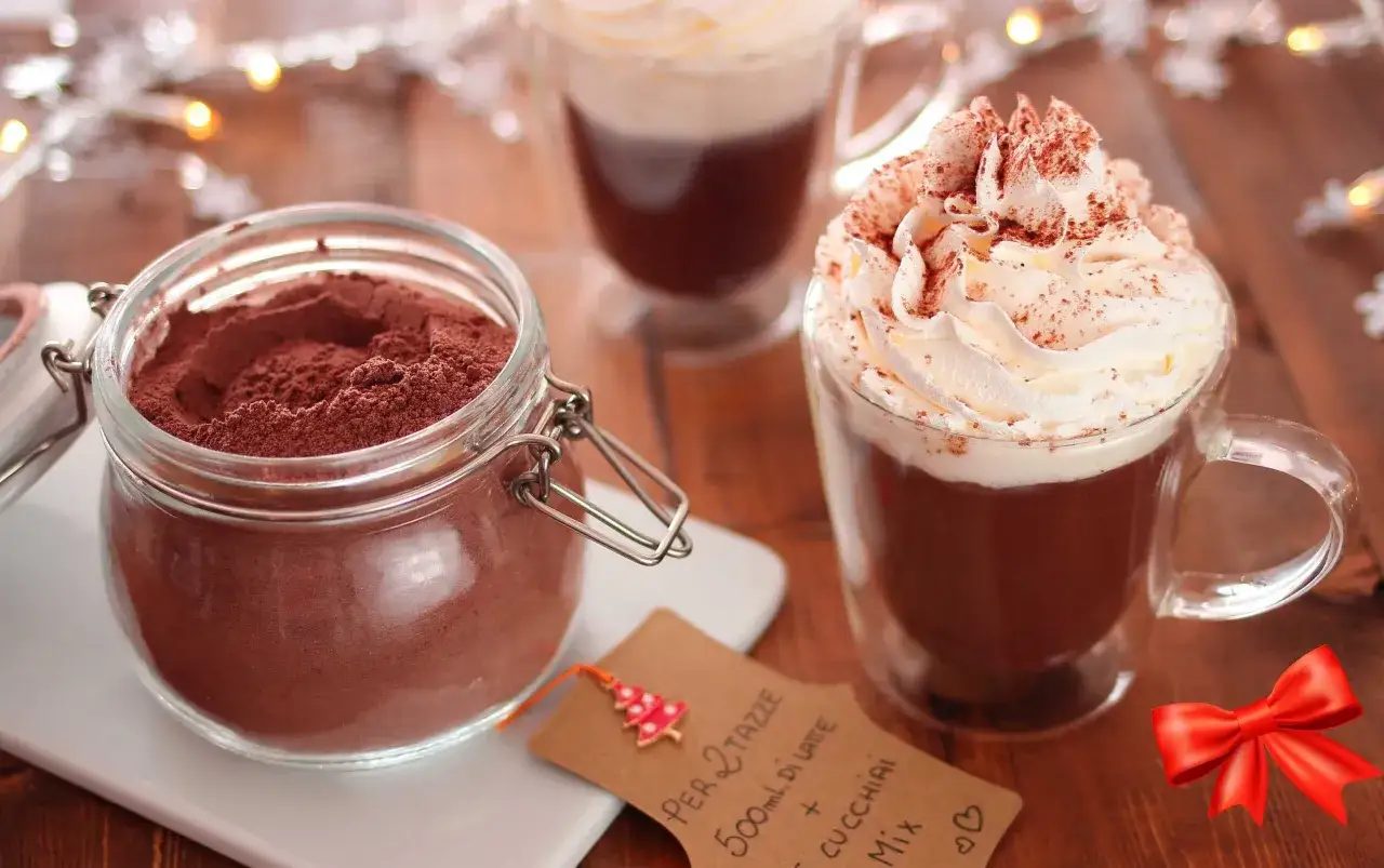 Un barattolo di cacao in polvere e due tazze di cioccolata calda con panna montata, perfette per imparare come fare una buona cioccolata calda.