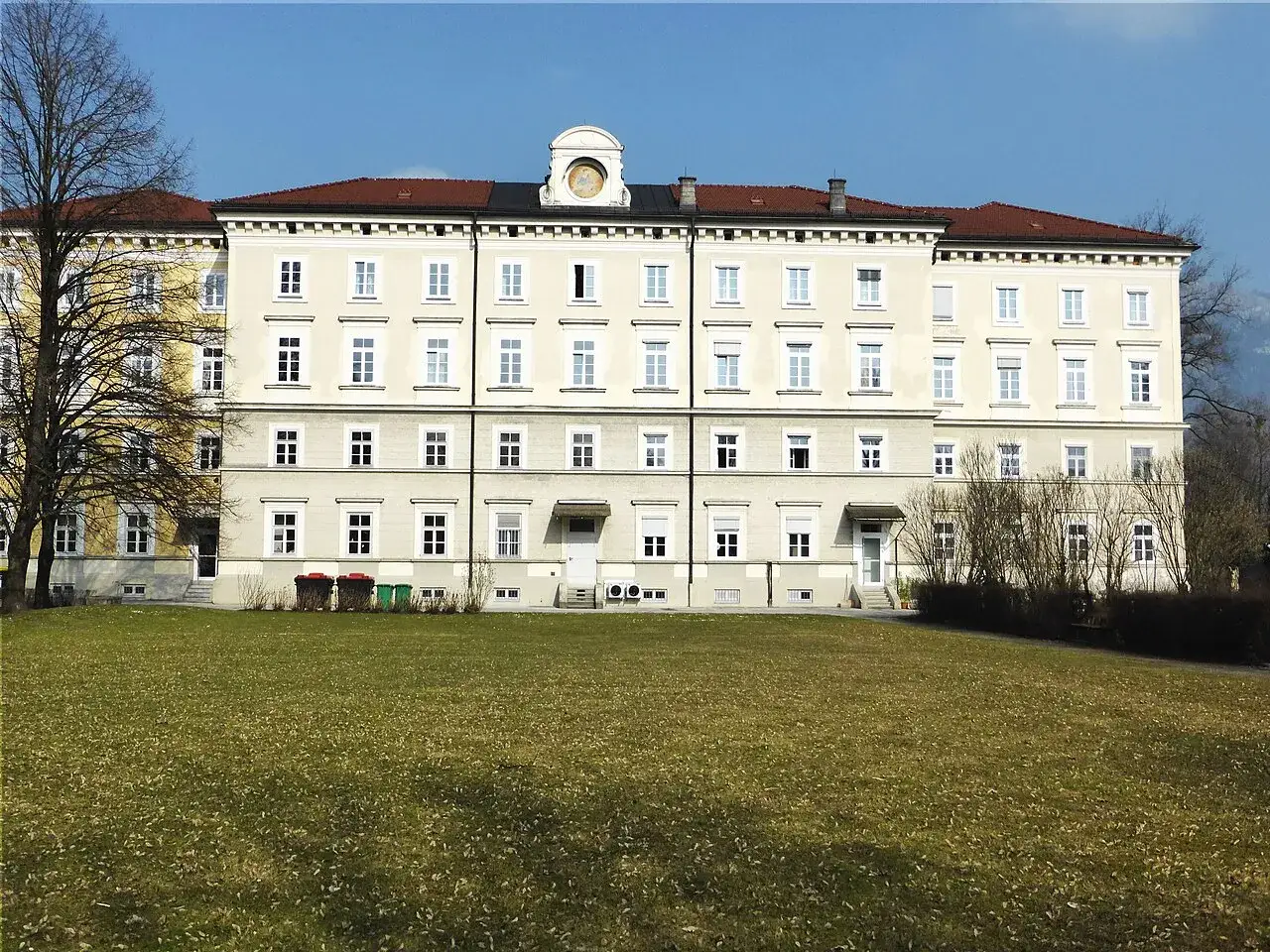 Großes Gebäude mit vielen Fenstern, das an ein Kloster in Salzburg erinnert. Ein gepflegter Rasen davor.