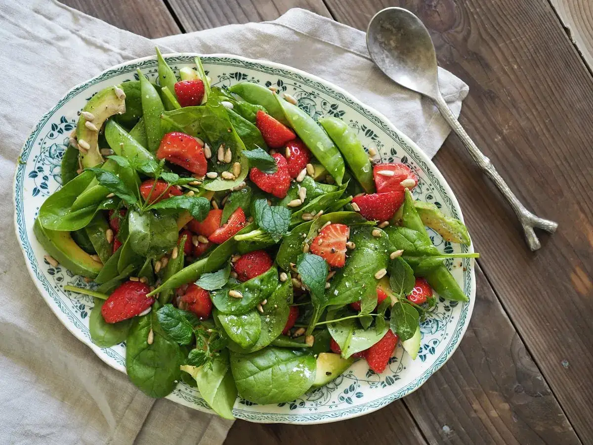 En härlig somrig sallad med spenat, jordgubbar, avokado och sockerärtor, toppad med solrosfrön.