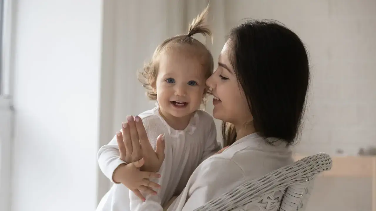 Madre sonríe mientras su bebé, que empieza a balbucear, le da la mano.