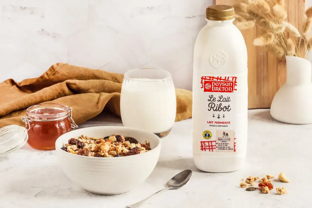 Un petit-déjeuner sain avec un bol de granola, un pot de confiture, un verre de lait ribot et une bouteille de lait ribot.