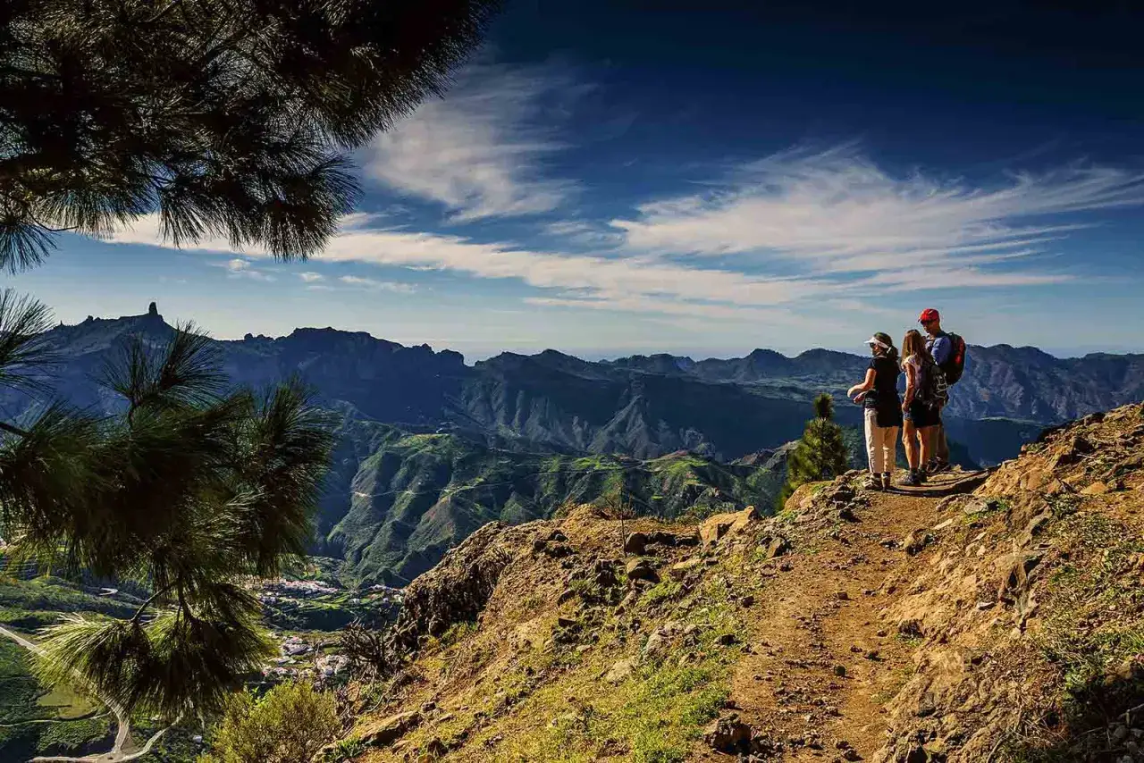 Familia disfrutando de unas caminatas en Gran Canaria, con vistas espectaculares de monta&ntilde;as y un pueblo al fondo.