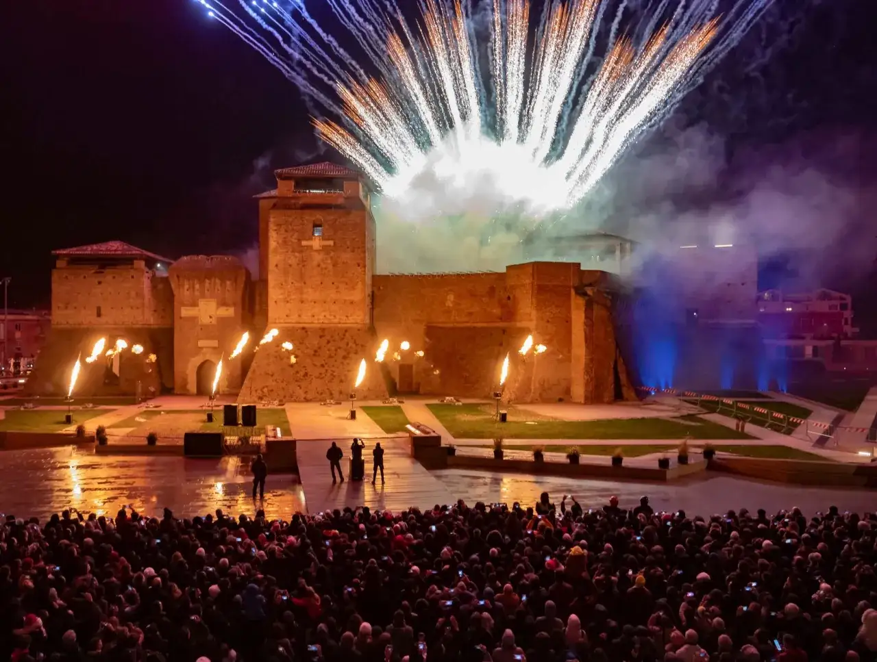 Spettacolare **capodanno in riviera romagnola** con fuochi d'artificio che illuminano un castello medievale, mentre una folla festante ammira lo show.