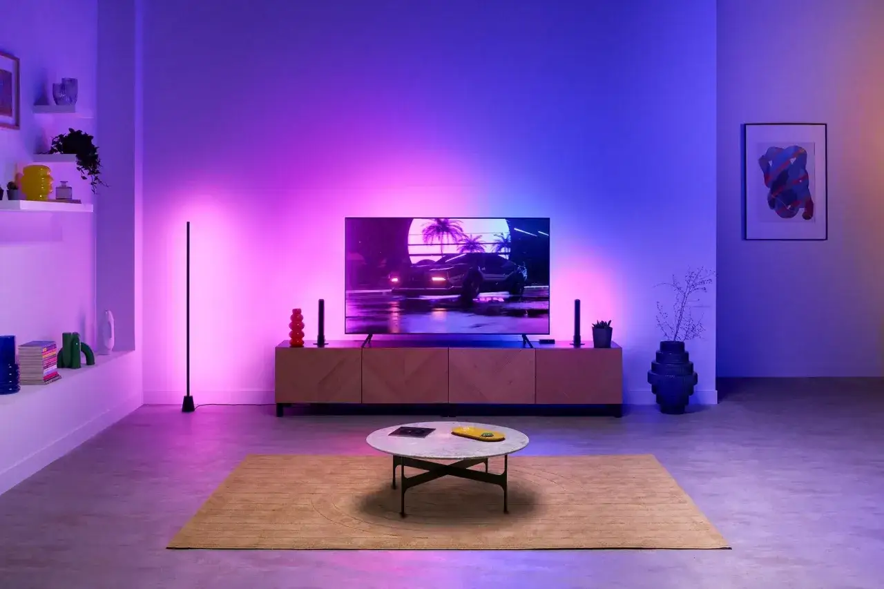Modernes Wohnzimmer mit einem Fernseher, der ein Auto-Motiv zeigt, umgeben von stimmungsvollem lg ambilight in Lila- und Blautönen.