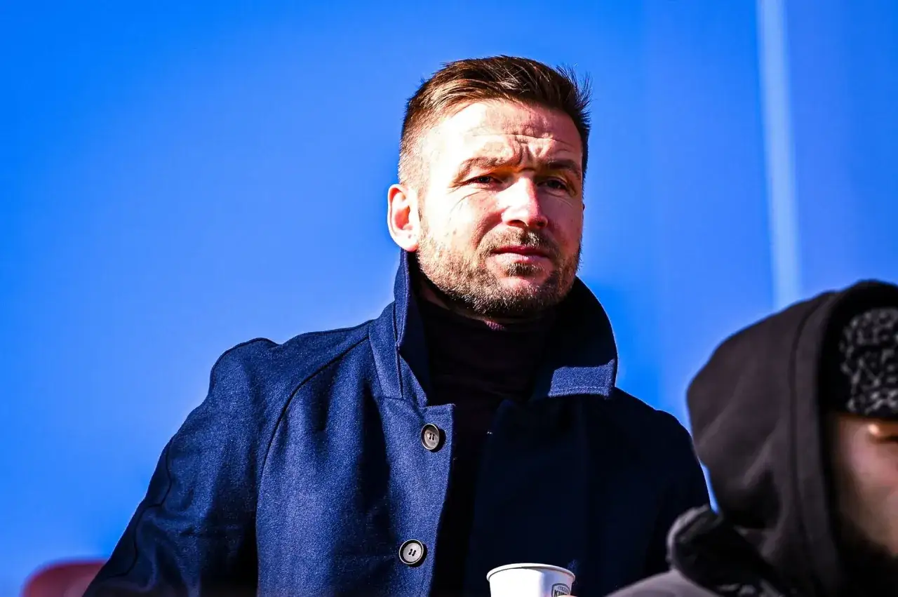 Skupiony piast gliwice trener w granatowym płaszczu, z niebieskim niebem w tle.