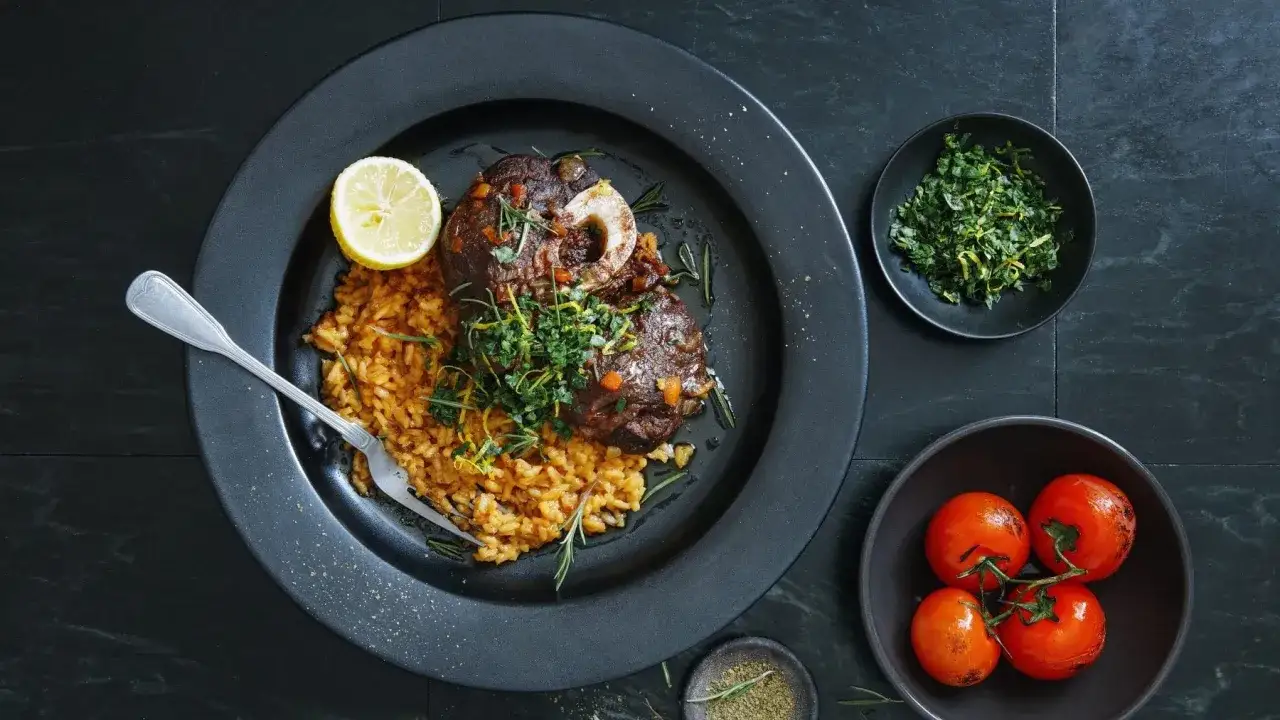 Ein köstliches Ossobuco Rezept mit zartem Kalbshaxenfleisch auf Safranrisotto, garniert mit frischen Kräutern und Zitrone.