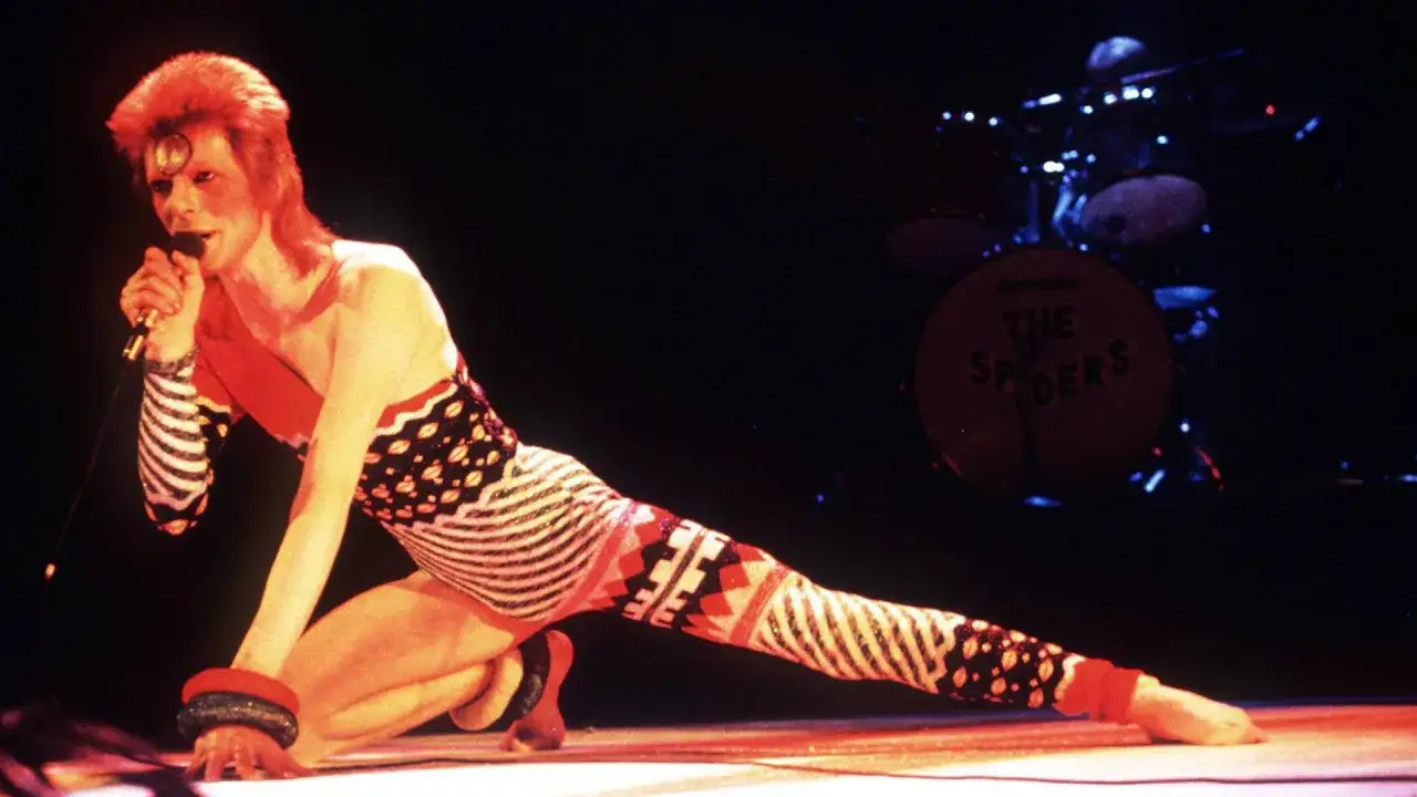 David Bowie in einem extravaganten Outfit auf der Bühne, die Energie der Drogen und des Rock'n'Roll in seiner Performance.