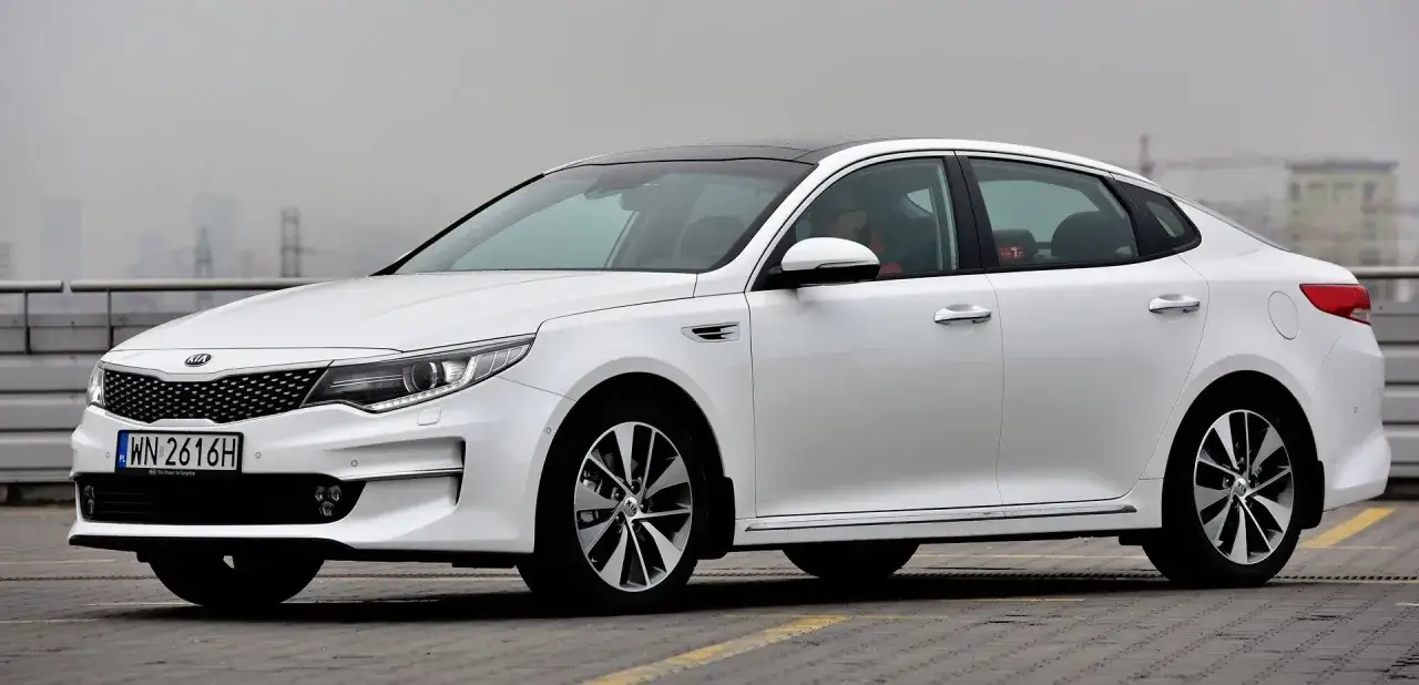 Biały kia sedan z czarnym dachem, zaparkowany na szarym tle.