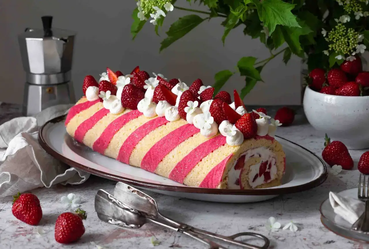Eine gestreifte Erdbeer-Biskuitrolle, dekoriert mit Sahnetupfern und frischen Erdbeeren, bereit zum Servieren.