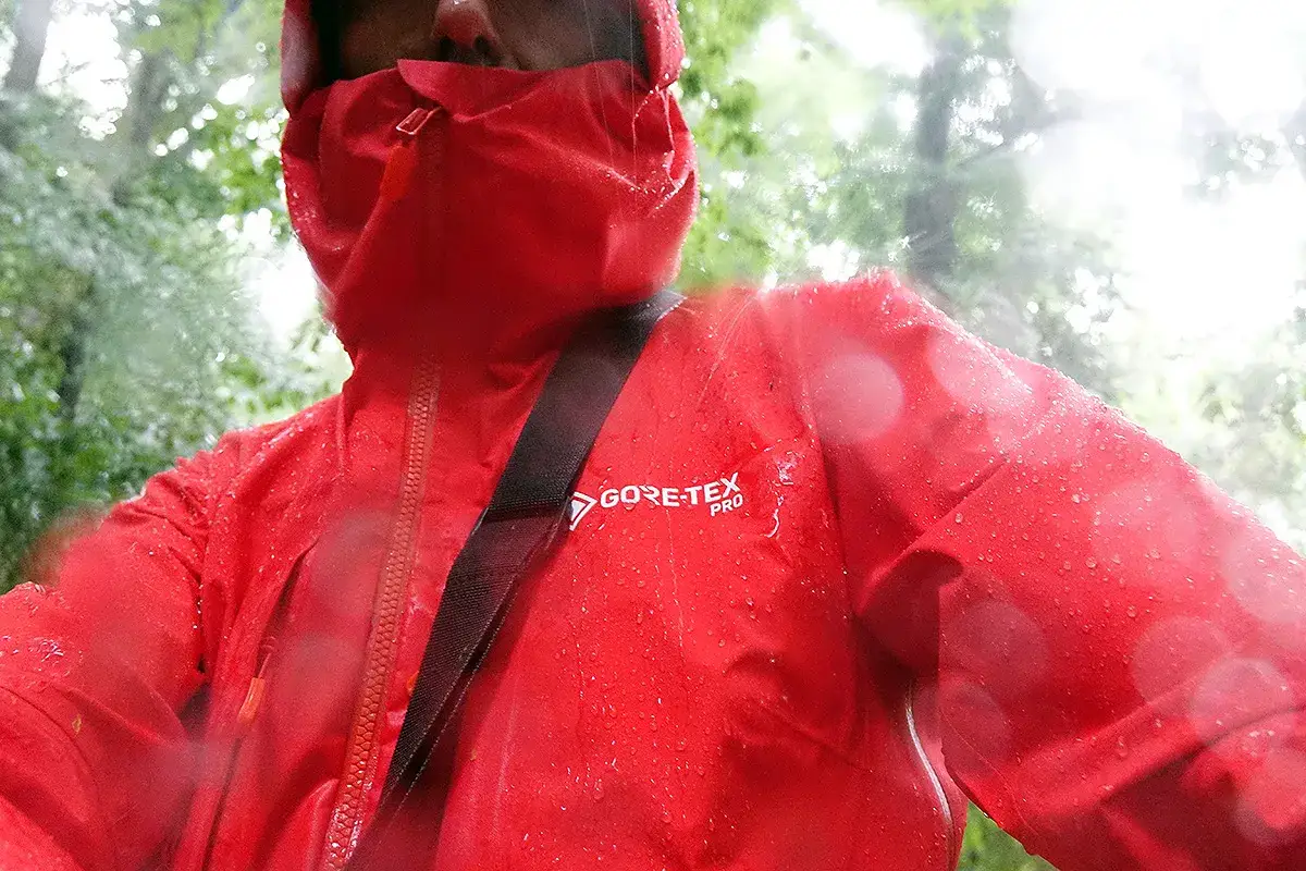 Czerwona kurtka z membraną GORE-TEX PRO chroni przed deszczem. Krople wody spływają po materiale, który pozostaje suchy.
