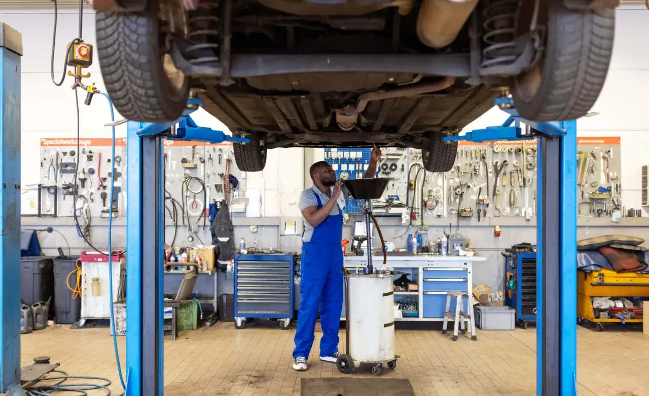 Mecánico realizando cambio de aceite a un coche elevado. Consulta el precio cambio de aceite para tu vehículo.