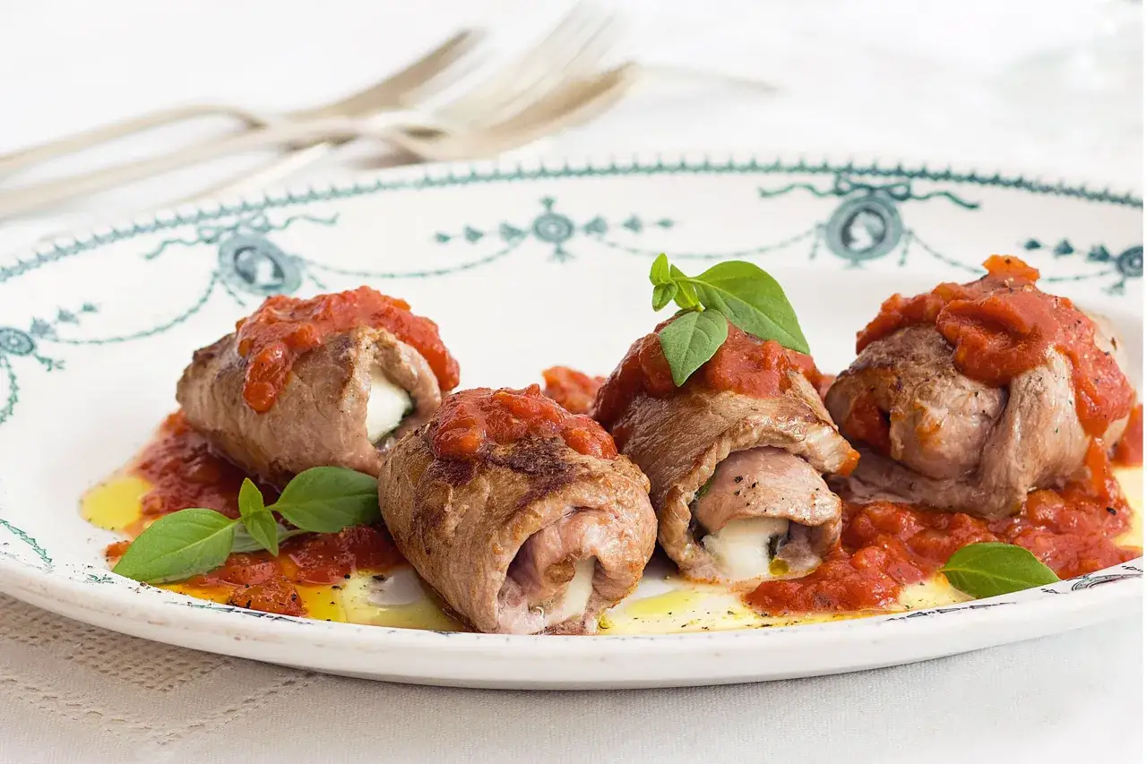 Quatre involtini de veau savoureux, garnis de fromage fondant, nappés de sauce tomate et décorés de basilic frais, sur une assiette ornée.