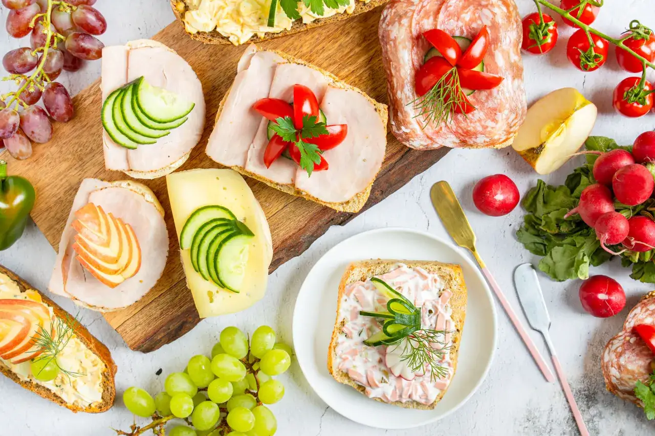 Vielf&auml;ltige Sandwich-Ideen mit Schinken, K&auml;se, Wurst, Ei und frischem Gem&uuml;se. Dazu Trauben, Radieschen und ein Apfel.