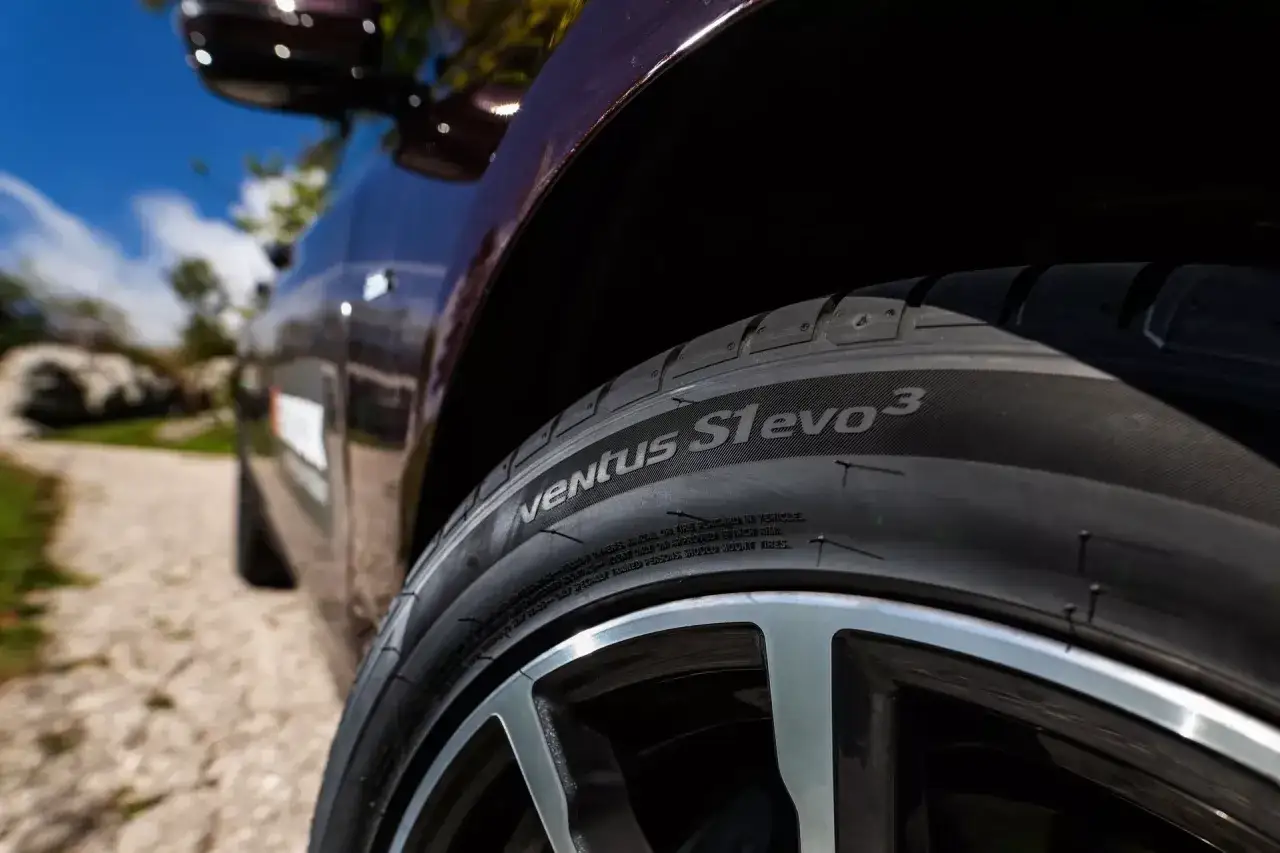 Nahaufnahme eines Hankook Ventus S1 evo 3 Reifens auf einem Auto. Der Reifen ist auf einer Schotterstra&szlig;e zu sehen.