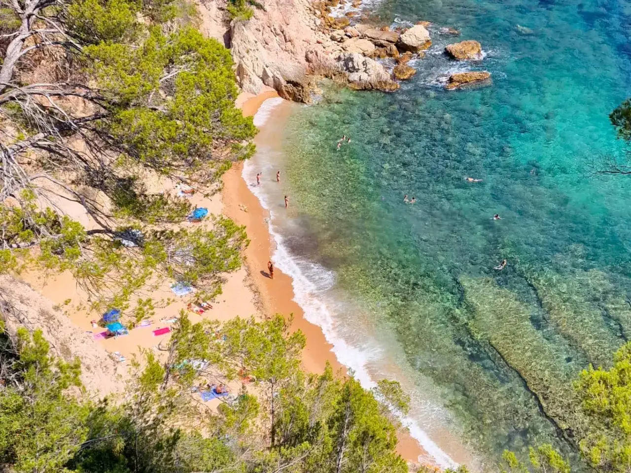 Una cala id&iacute;lica con arena dorada, aguas cristalinas y gente disfrutando del mar. Los **caminos de ronda** ofrecen vistas espectaculares de este para&iacute;so.