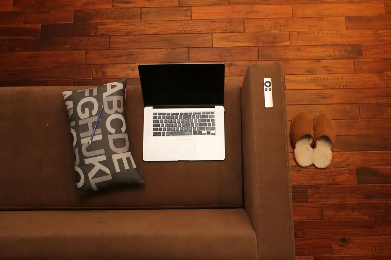 Na kanapie laptop, poduszka z literami i kapcie. Zastanawiasz się, **couchsurfing co to**? To podróżowanie i poznawanie świata, nocując u lokalnych ludzi.