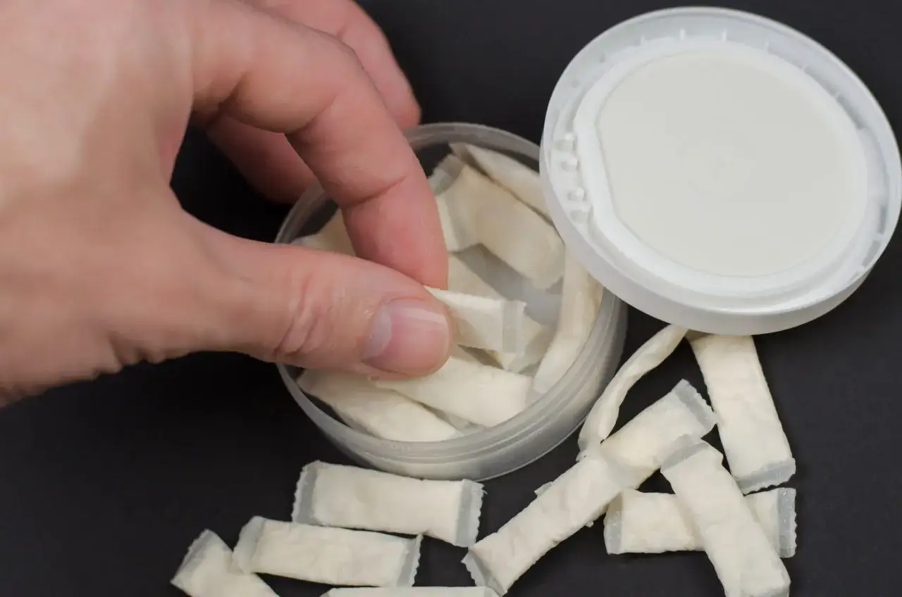 Dłoń sięga po białe saszetki. To snus, tytoń do ust w porcjach.