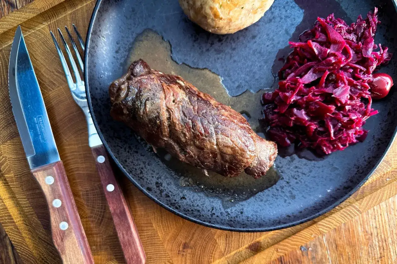 Herzhafte rouladen im dutch oven, serviert mit Rotkohl und Klößen auf einem rustikalen Teller.