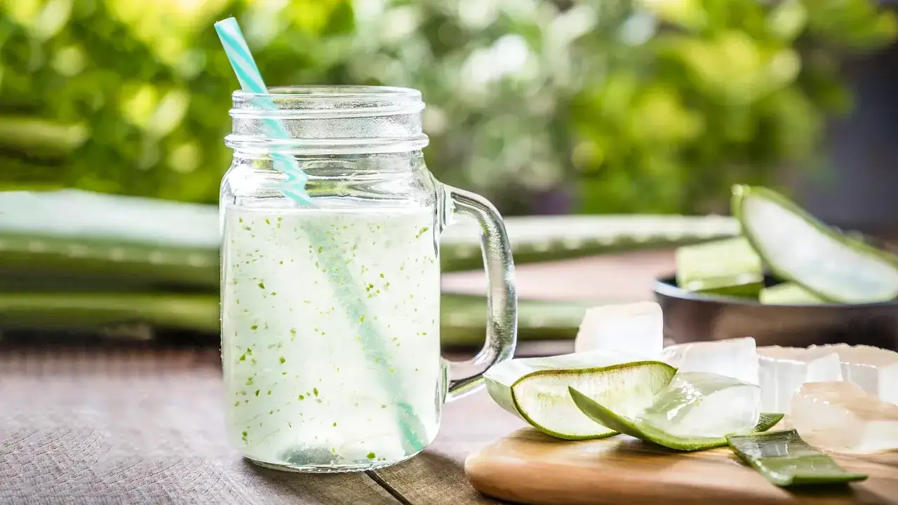 Un verre de **aloe vera à boire** rafraîchissant, avec des morceaux d'aloe vera frais sur une planche en bois.
