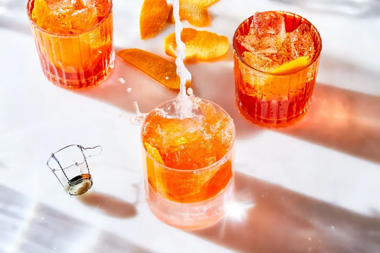 Erfrischender Aperitif mit Prosecco und Orangenzesten. Eisw&uuml;rfel sprudeln, w&auml;hrend der Schaumwein ins Glas flie&szlig;t.