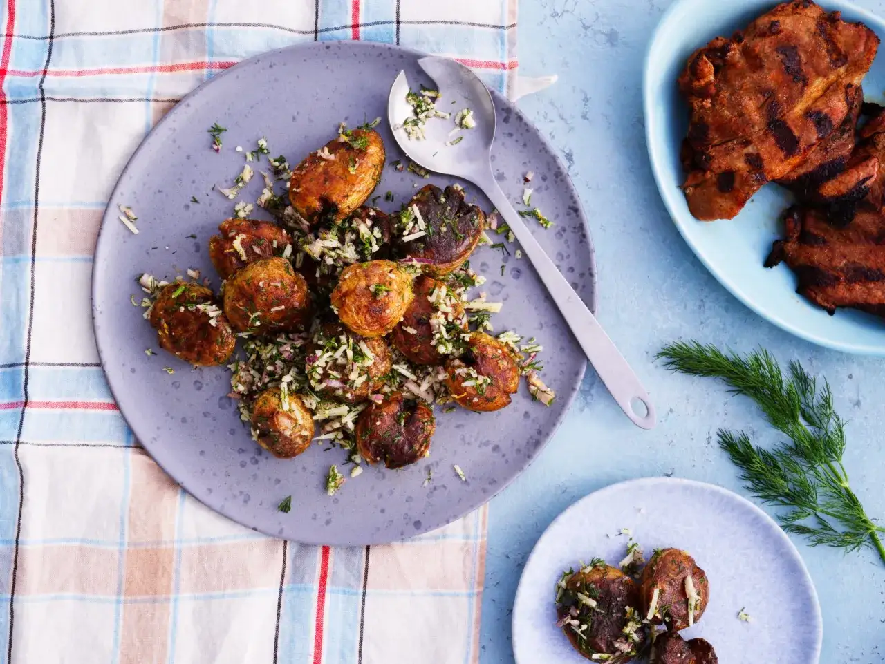 En tallrik med godaste potatissalladen, kryddad med dill och lök, bredvid grillad kött.