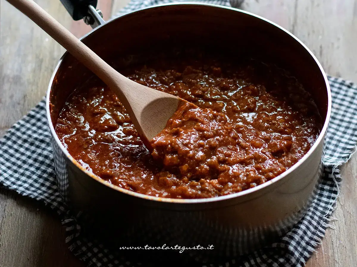 Un pentolone pieno di rag&ugrave; fumante, pronto per una ricetta perfetta. Un cucchiaio di legno mescola la salsa densa e saporita.