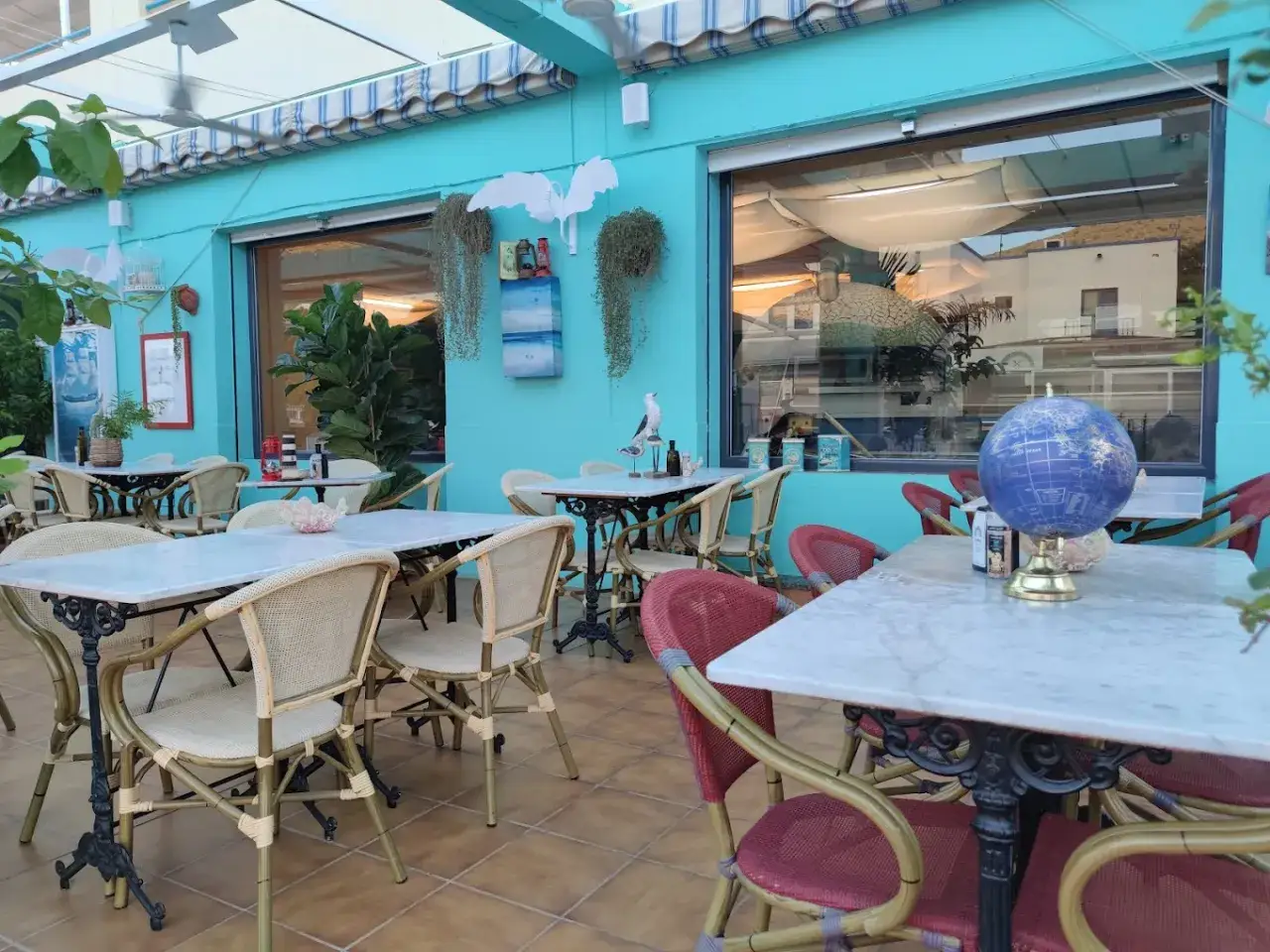 Terraza de restaurante con mesas y sillas, ideal para saber donde cenar en San José. Decoración náutica y un globo terráqueo.