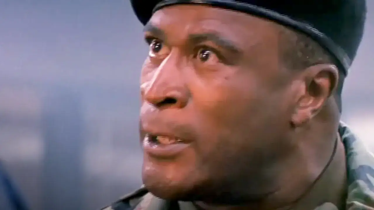En man i militärkläder och basker, en karaktär från rollistan i Die Hard 2, ser oroligt åt sidan.