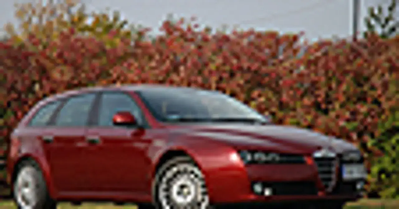 Czerwone Alfa Romeo 159 SW na tle jesiennych krzewów. Wiele pozytywnych alfa romeo 159 opinie potwierdza jego klasę.