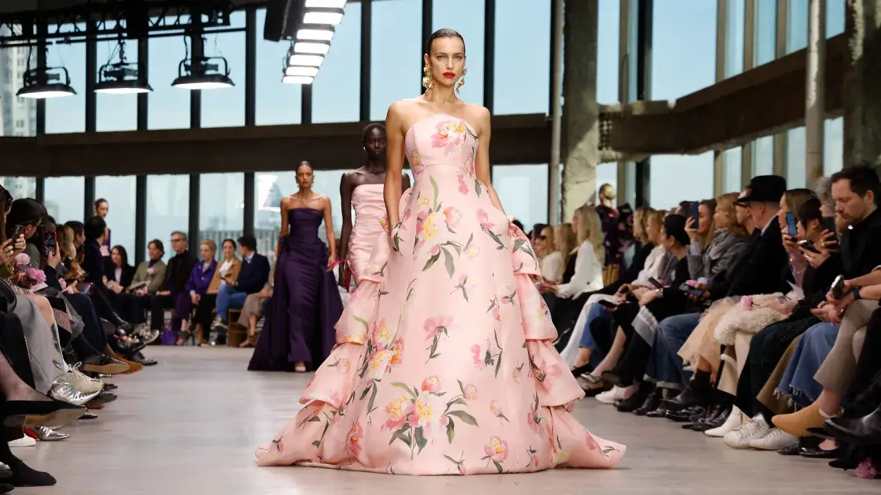 Desfile de Carolina Adriana Herrera: modelo luce un vestido rosa con flores, mientras el público observa.