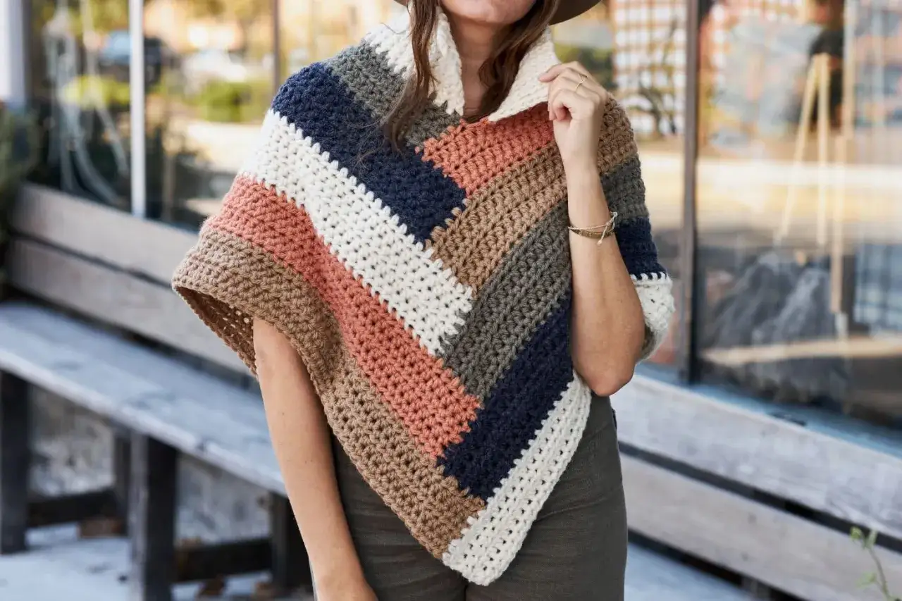 Poncho a crochet rectangular con rayas diagonales en tonos tierra, blanco y azul marino. Perfecto para un d&iacute;a fresco.