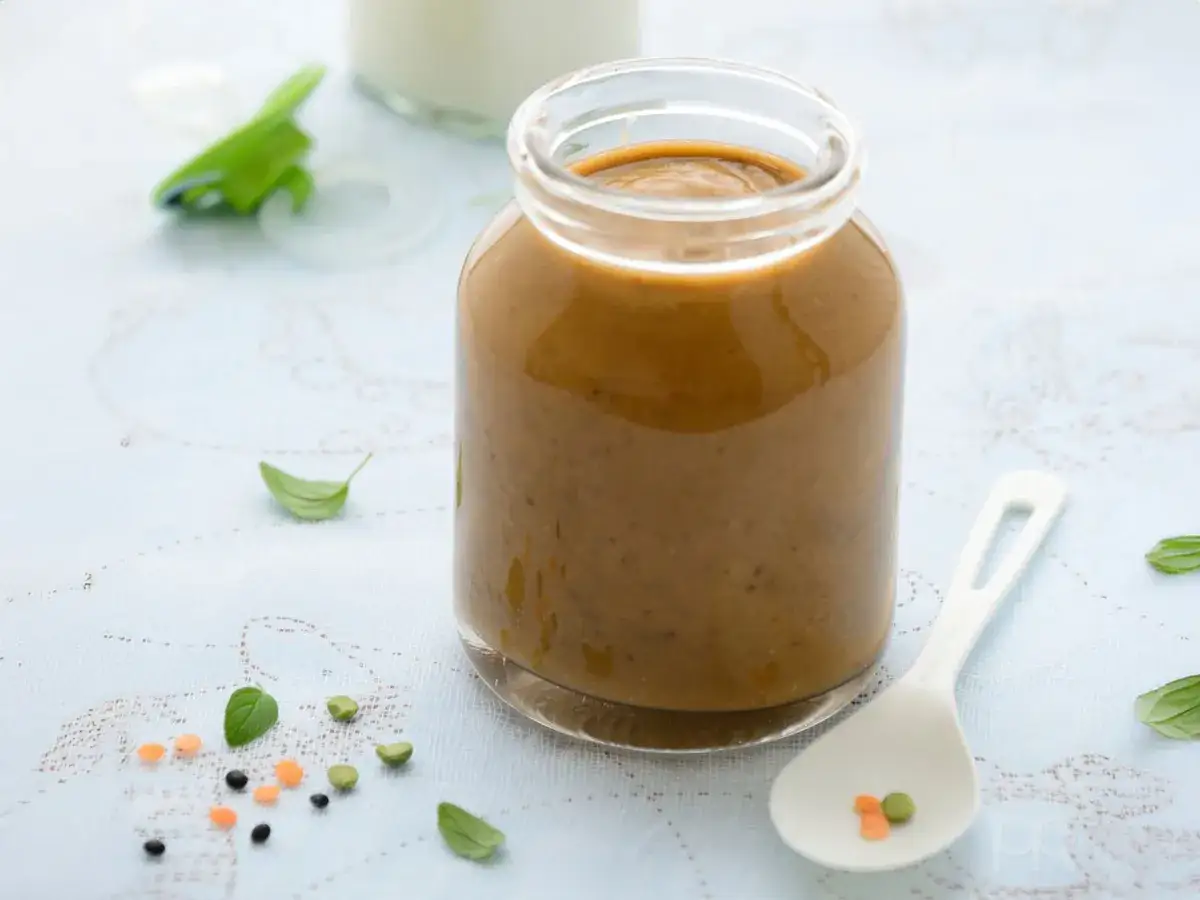 Tarro de lentejas bebé, con una cuchara y algunas lentejas sueltas. Ideal para la alimentación infantil.