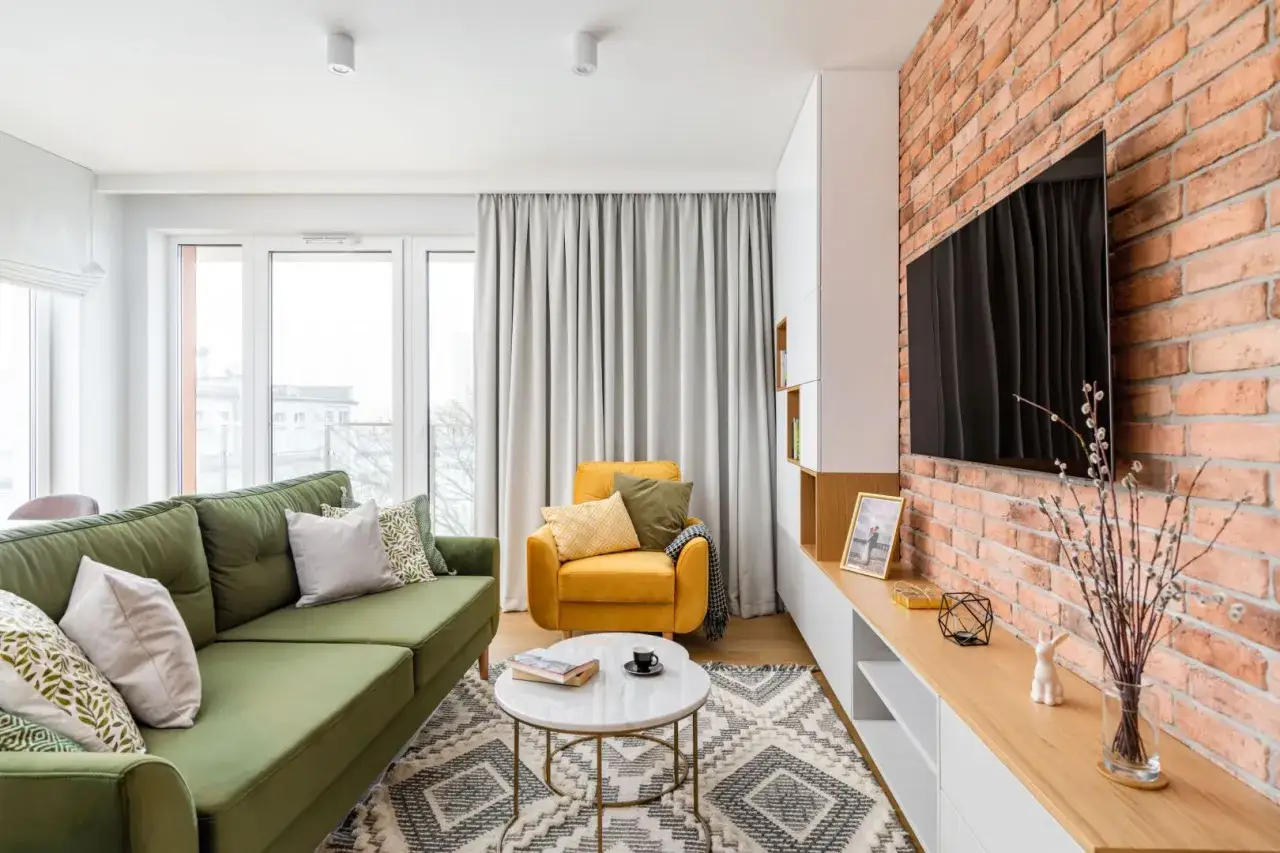 Zielona sofa i żółty fotel w salonie z ceglaną ścianą. Czy to sofa czy kanapa? Zależy od wielkości i przeznaczenia.