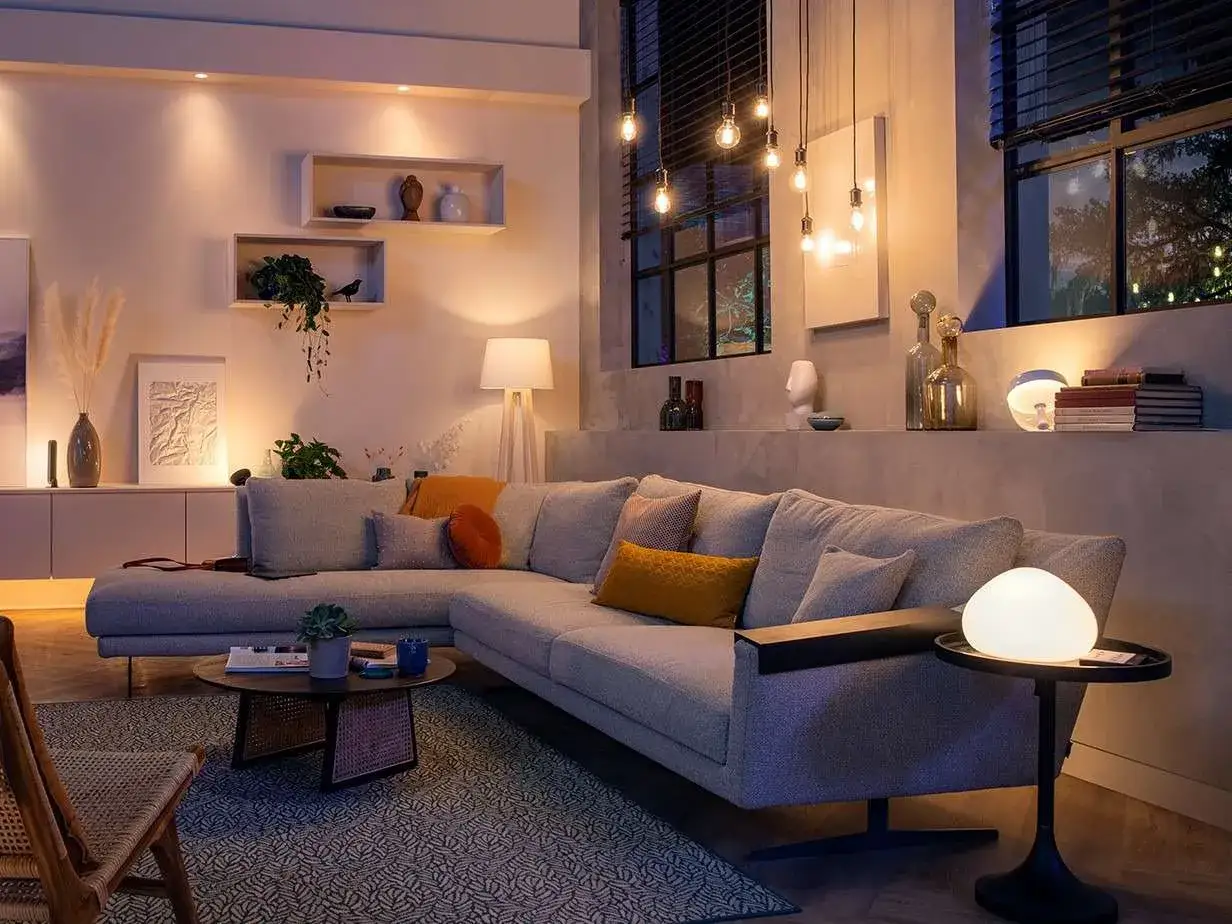 Un sal&oacute;n moderno con sof&aacute; gris, mesas de centro y l&aacute;mparas de techo y de mesa. Una gu&iacute;a de como iluminar un salon con luz c&aacute;lida y ambiental.