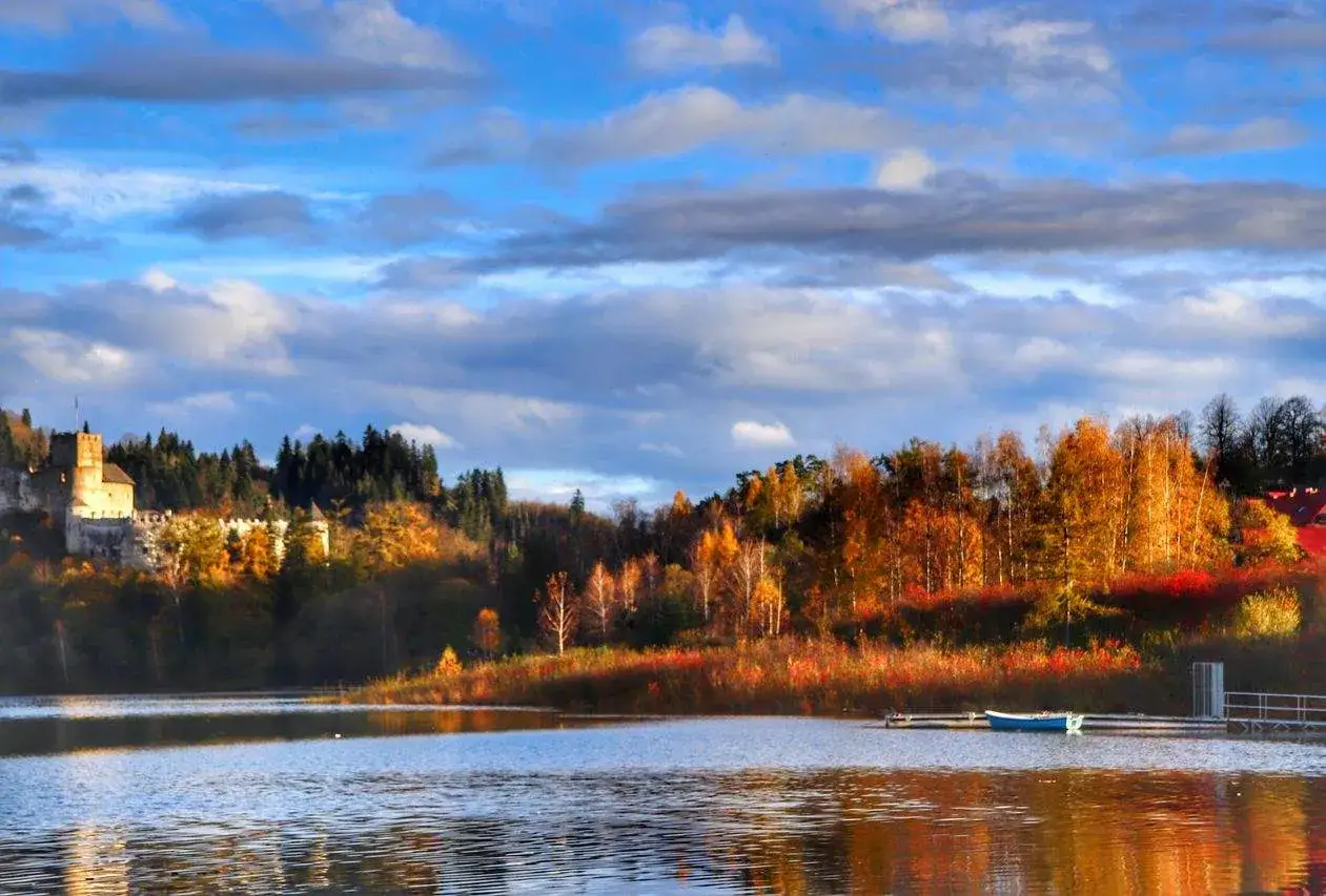 Zamek w Niedzicy w Małopolsce, otoczony jesiennymi barwami drzew, nad spokojną taflą jeziora.