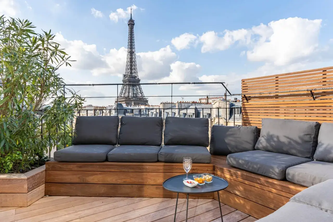 Terrasse parisienne avec vue sur la Tour Eiffel. Canapés confortables, table basse avec apéritifs. Un vrai complément de loyer pour profiter de la vie parisienne.