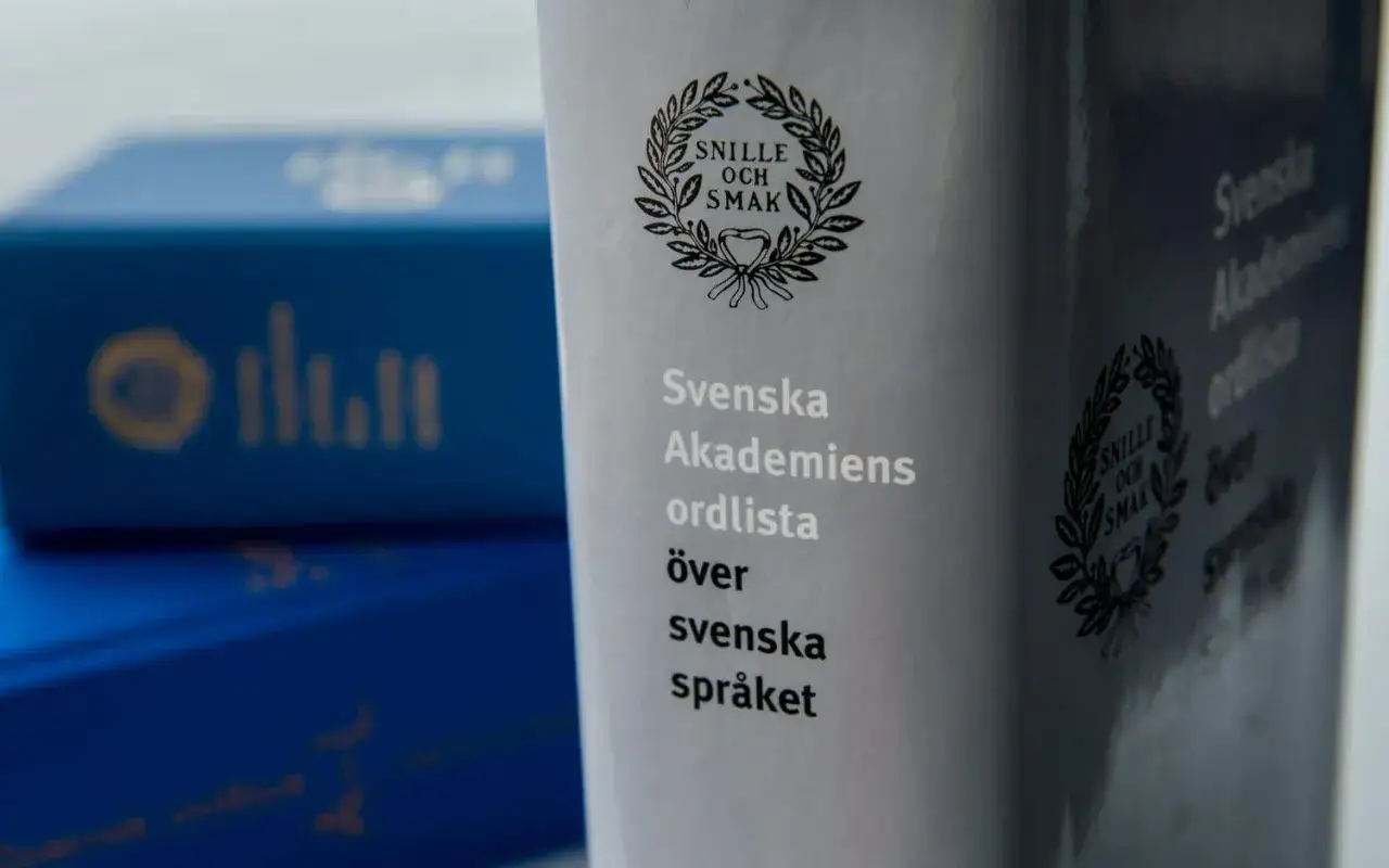 Svenska Akademiens ordlista över svenska språket. Blå askar med gul text syns i bakgrunden, som om de väntar på att få veta vart eller blev.