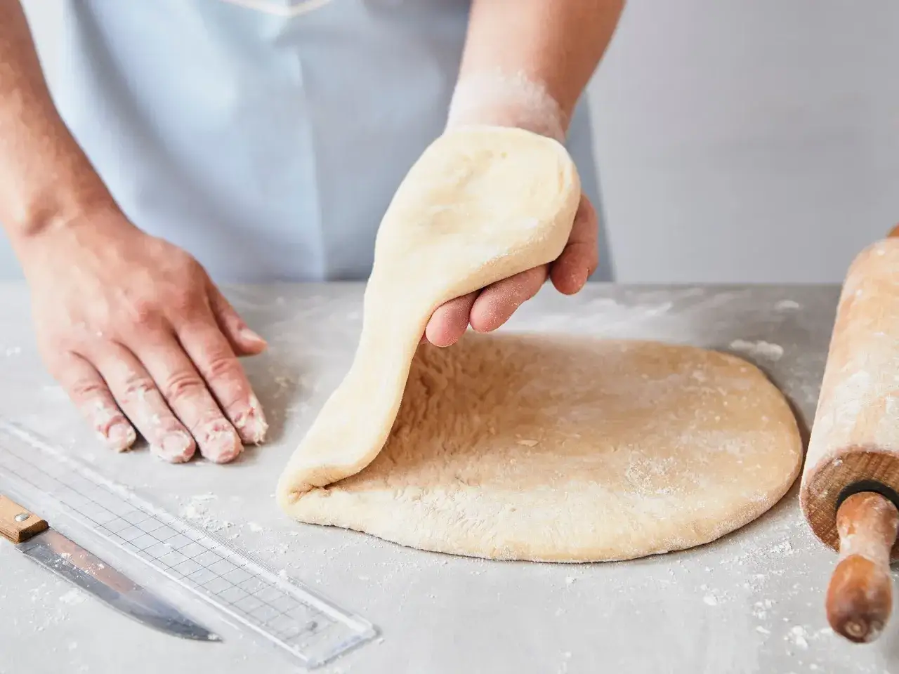 Hände kneten Teig für ein Schmalzkuchen Rezept. Ein Nudelholz und ein Messer liegen bereit.