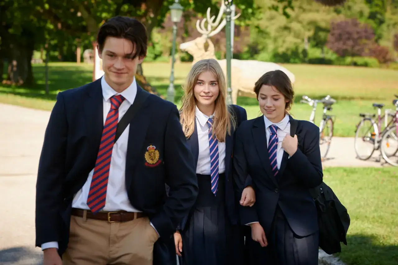 Drei Sch&uuml;ler in Schuluniformen gehen l&auml;chelnd durch einen Park. Ein Hirsch-Dekor im Hintergrund erinnert an die serie gestern waren wir noch kinder.