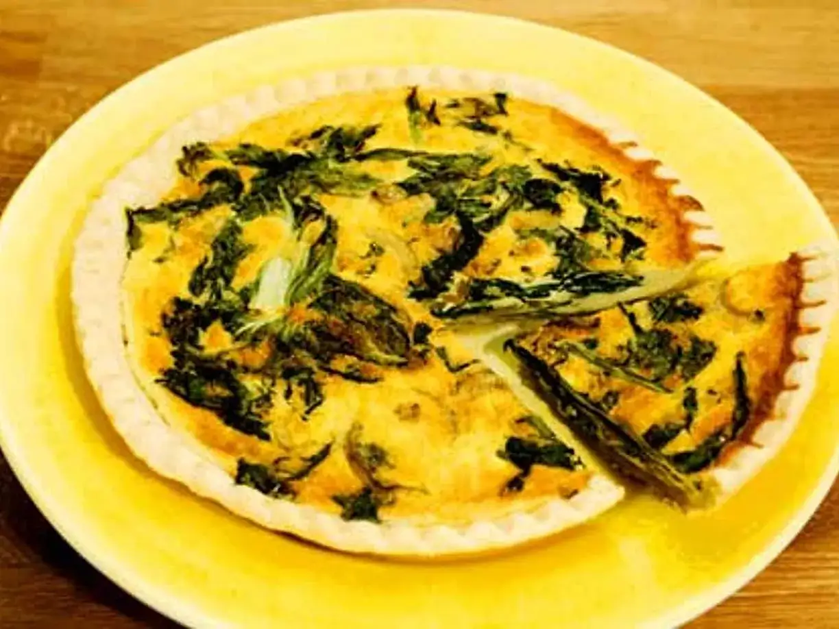 En gyllene, smakrik vegetarisk paj med spenat och ägg, serverad på en gul tallrik. En bit är uppskuren.