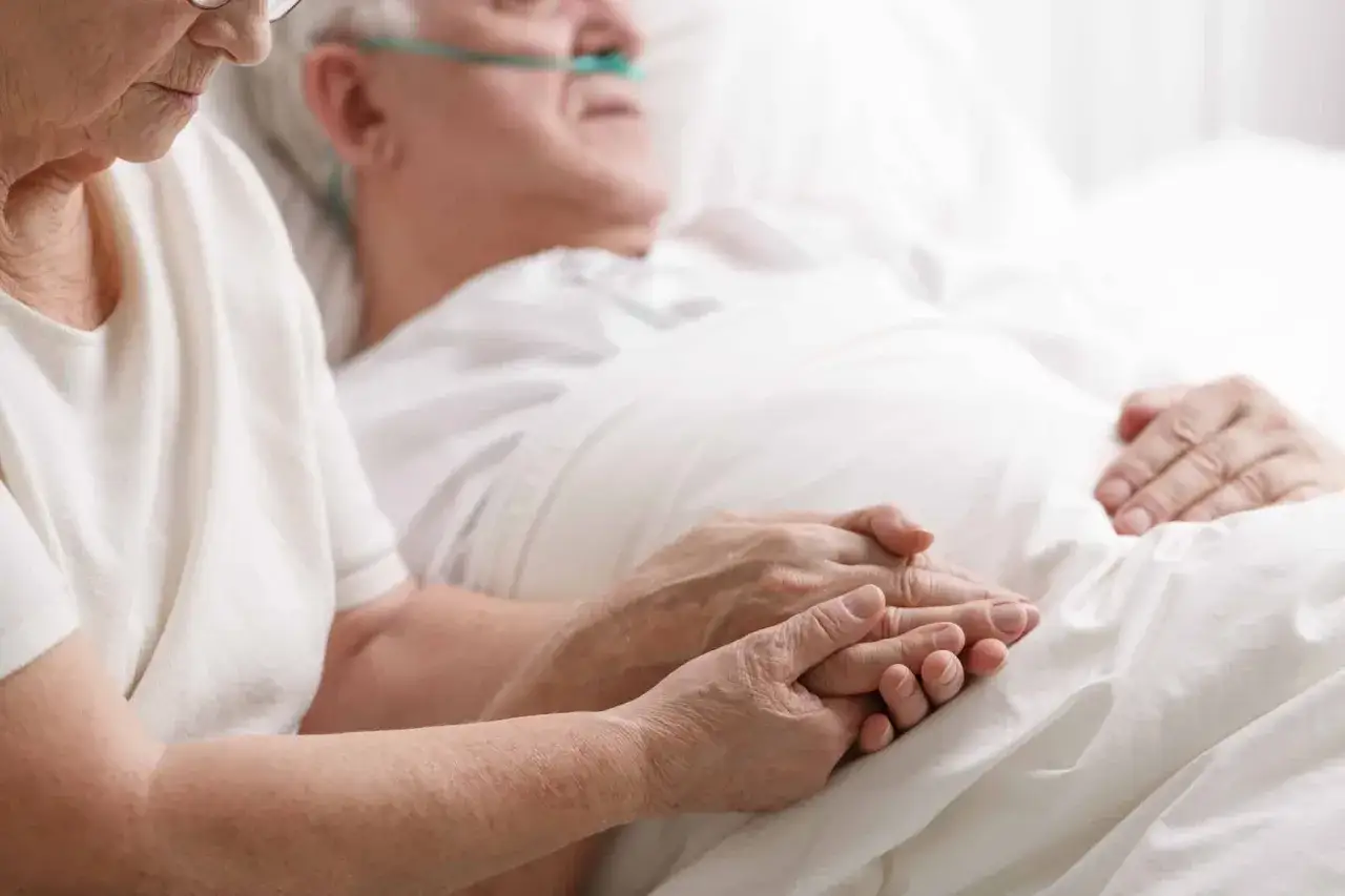 Eine Frau hält die Hand eines Mannes im Krankenhausbett, der Sauerstoff erhält. Die Frage welcher Pflegegrad bei Palliativ ist hier zentral.