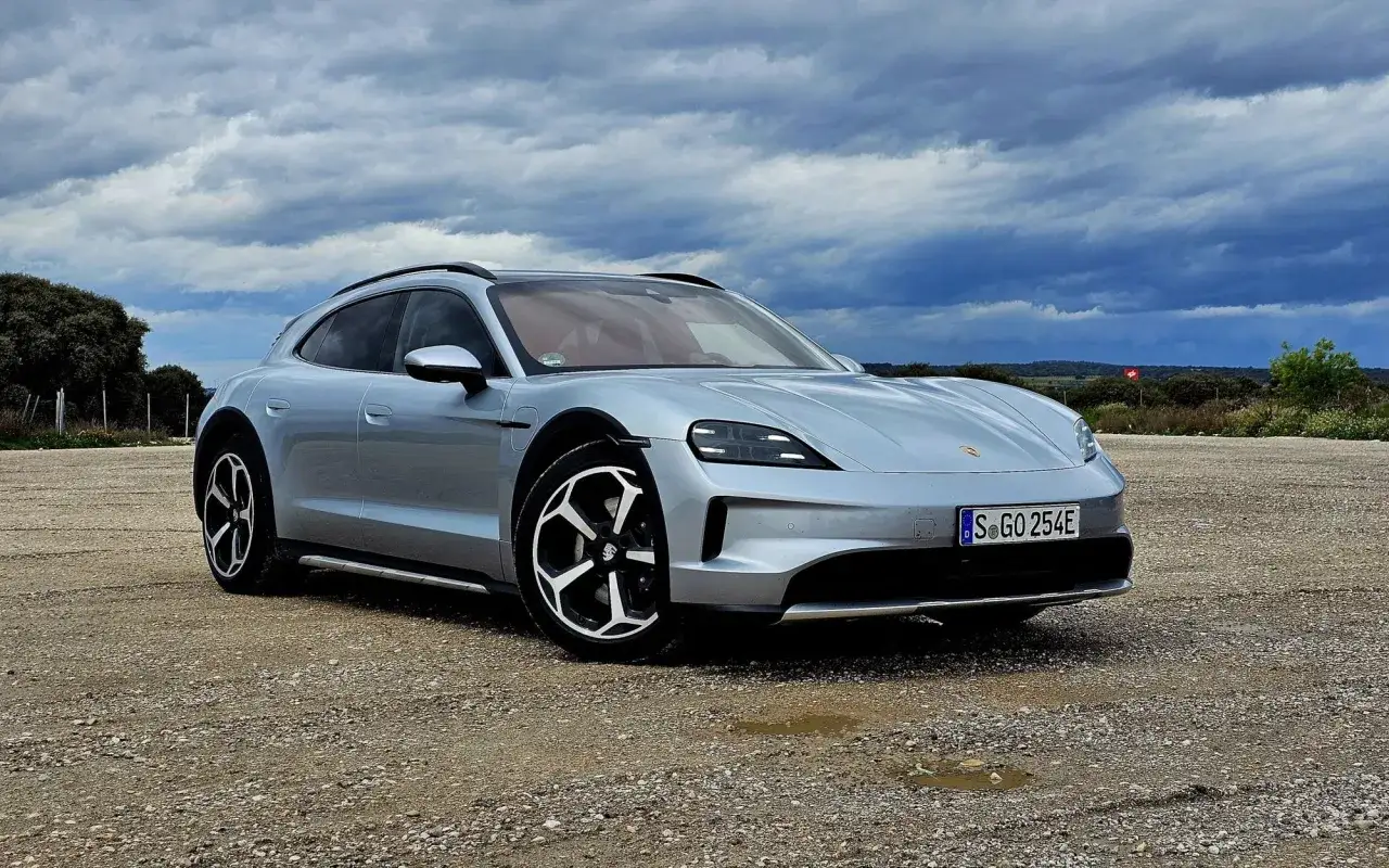 Srebrny Porsche Taycan Cross Turismo na żwirowym podjeździe, pod burzowym niebem.